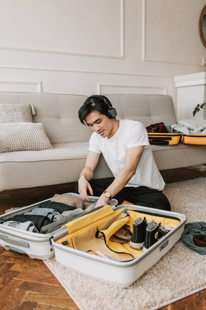 Young man packing suitcase in living room while listening to music.